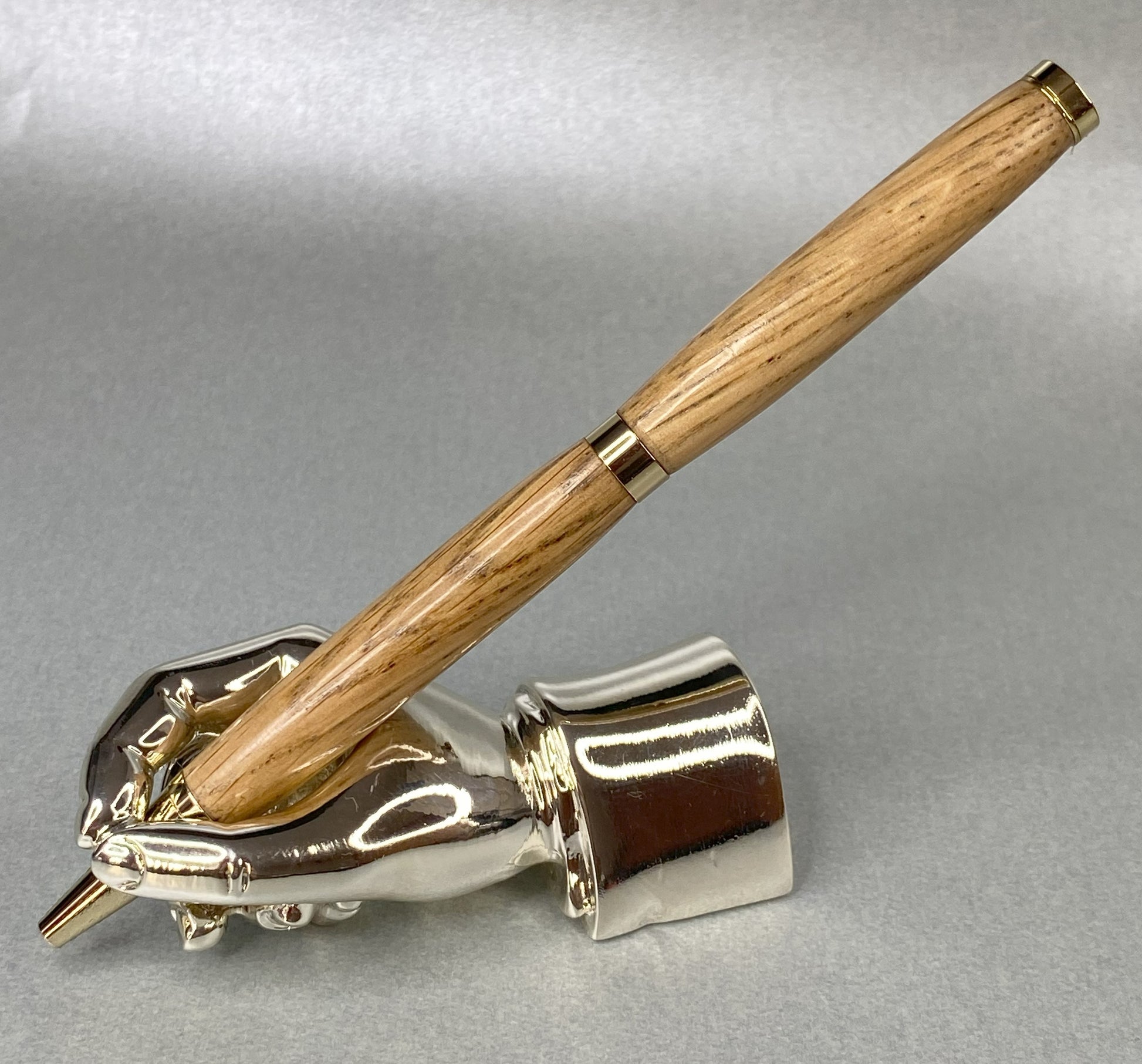 English Oak wood pen standing on a left handed chrome hand in gold plated fittings showing the back of the pen