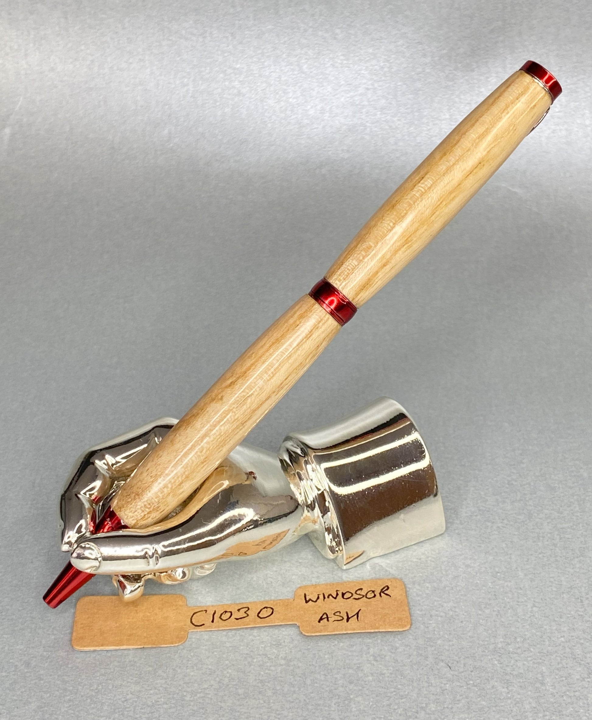 Ash wood pen with red plated fittings  standing on a chrome plated hand shape