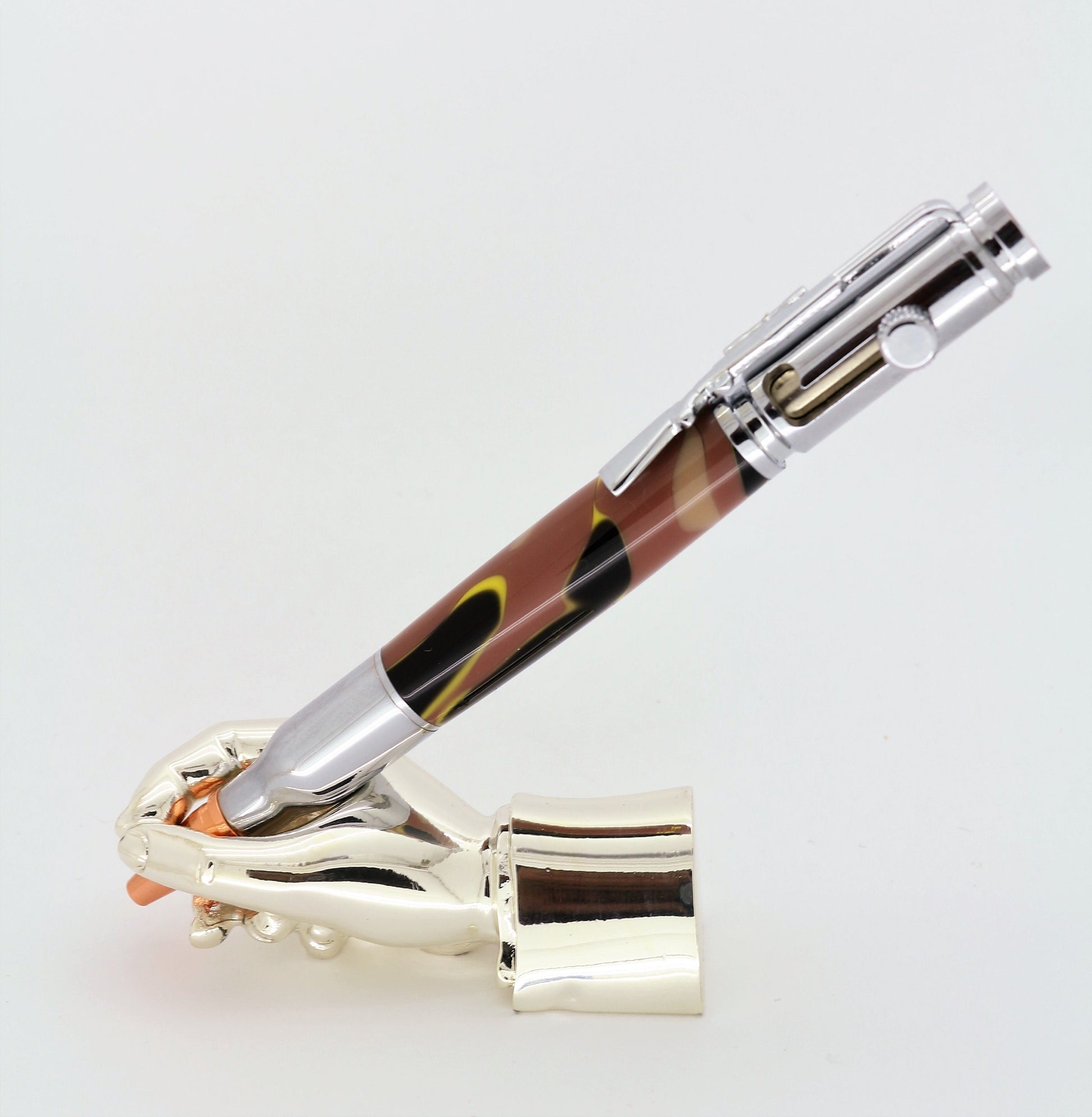 A right hand shaped metal base holding a handturned yellow cammo acrylic Bolt action pen as you would hold it to write with.