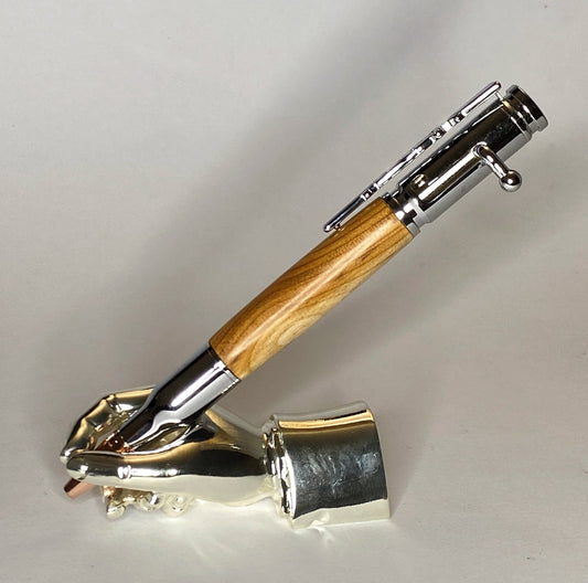A right hand shaped metal base holding a handturned Yew Wood Bolt action pen as you would hold it to write with.