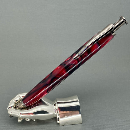 A right hand shaped metal base holding a handturned Red and Blacl acrylic pen as you would hold it to write with. Showing its Chrome plating and the clicker at the pen top to operate the nib.