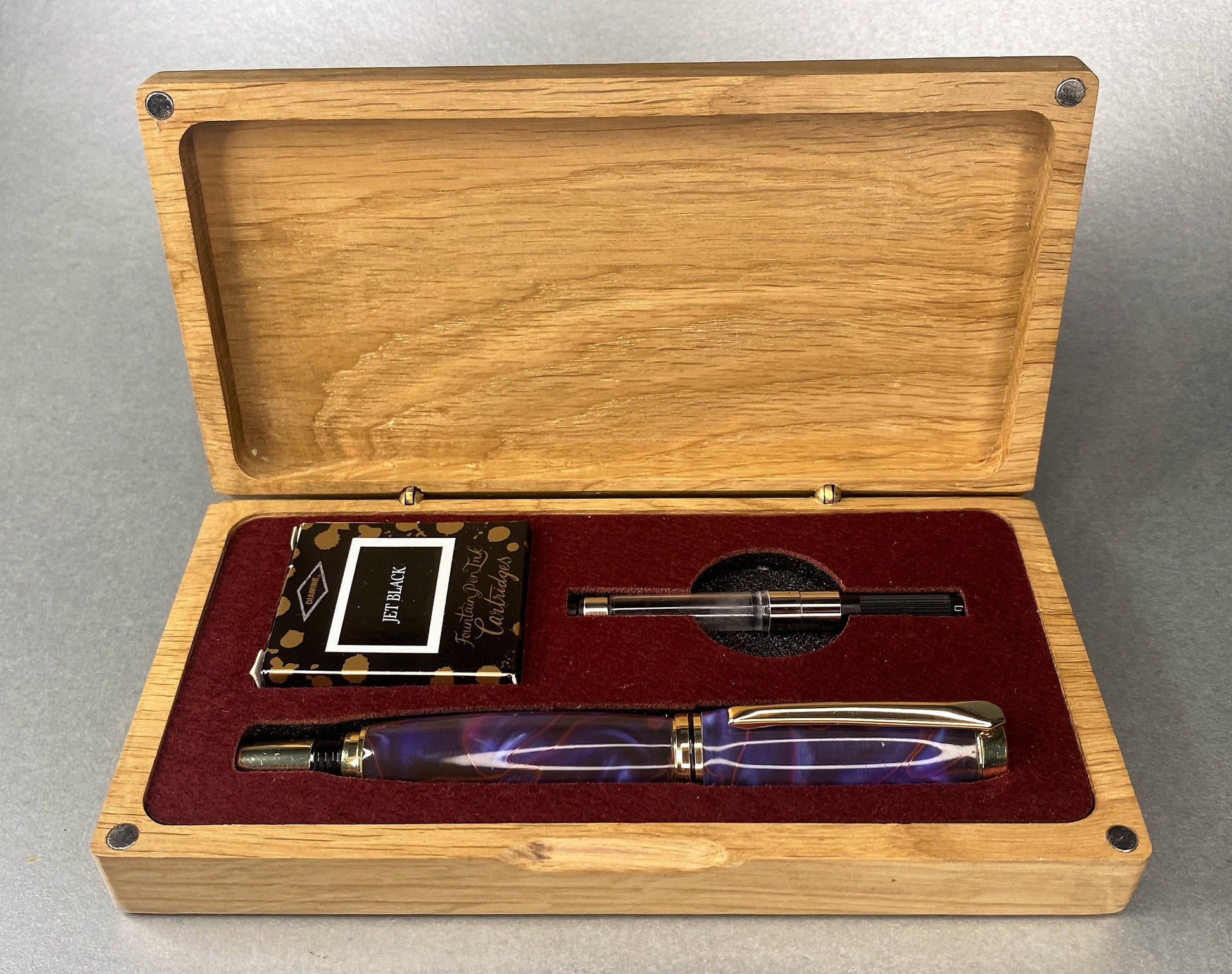 Open lidded Oak box showing a Purple & red stripe effect Acrylic Fountain pen the pen has Gold plated fittings