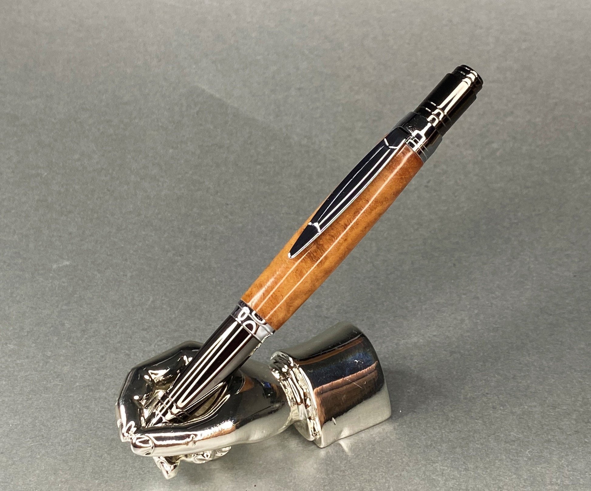 A right hand shaped metal base holding a handturned Jarrah burr Wood pen as you would hold it to write with.